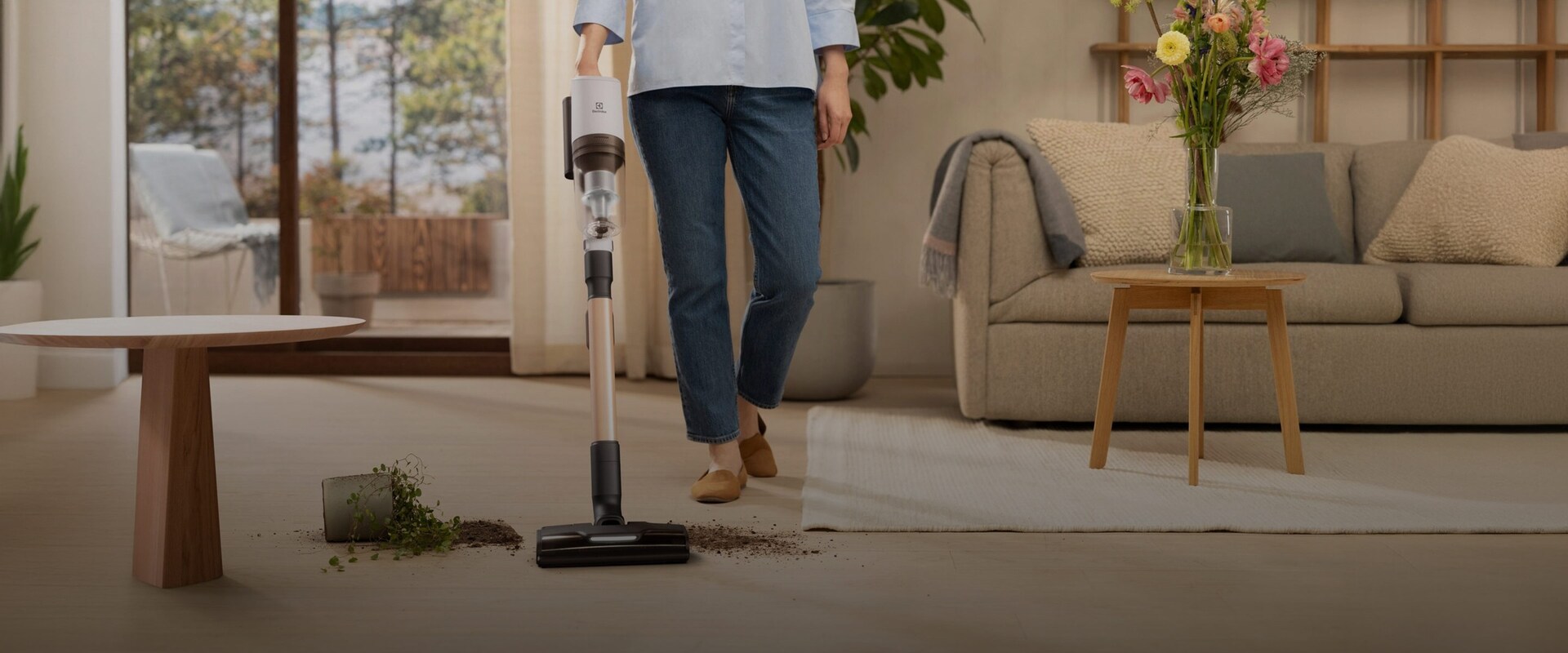 En kvinde støvsuger jord op fra gulvet med en Electrolux ledningsfri støvsuger.